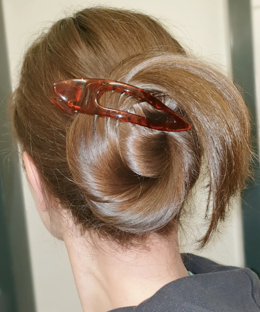 A woman with shiny brunette hair wears a sleek twisted bun accented with a horizontal arrow shaped tortoiseshell claw clip.