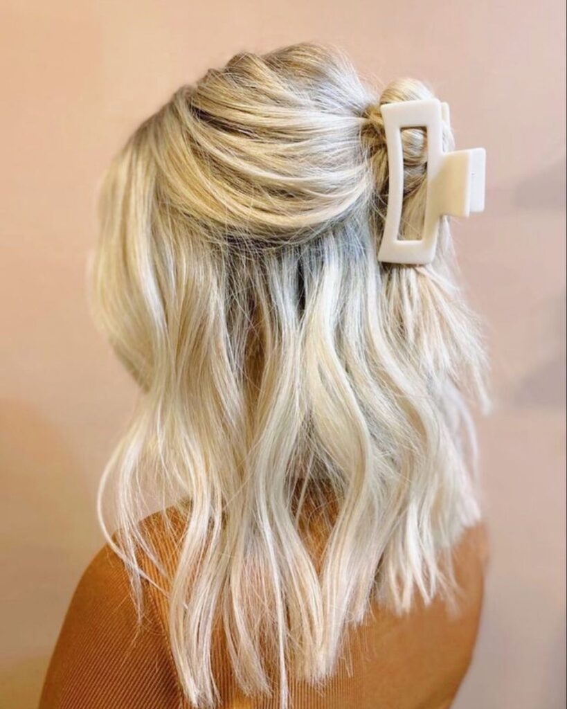 Medium-length wavy blonde hair styled in an effortless half-up twist and secured with a cream-colored rectangular claw clip.