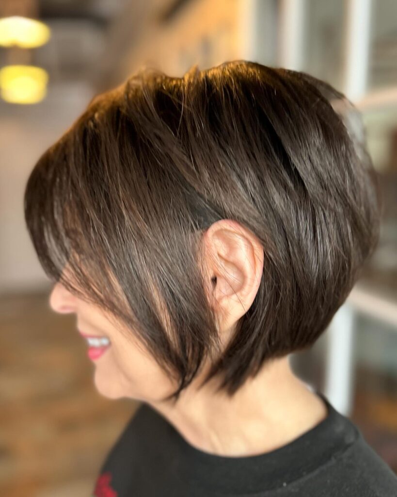 A smiling woman with a chocolate brown pixie bob tucked behind one ear is shown in profile.