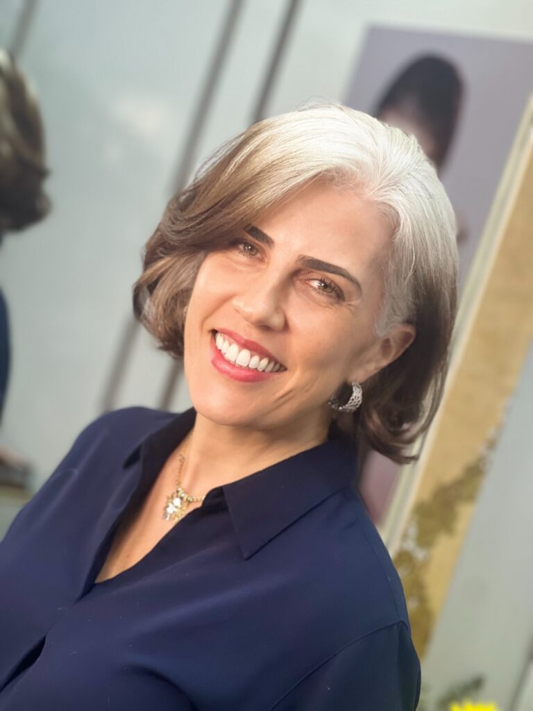A smiling woman with a voluminous curled bob featuring bright blonde and deeper root color tones.