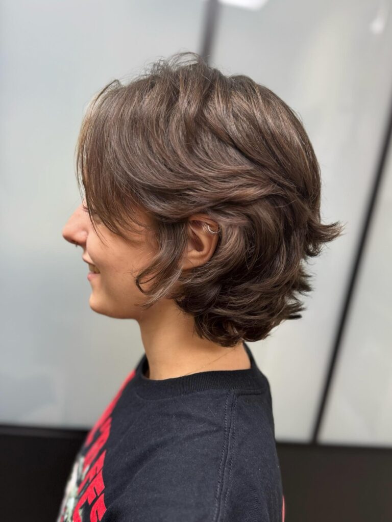 A woman with a voluminous chestnut brown bob featuring flipped out ends is shown in profile.