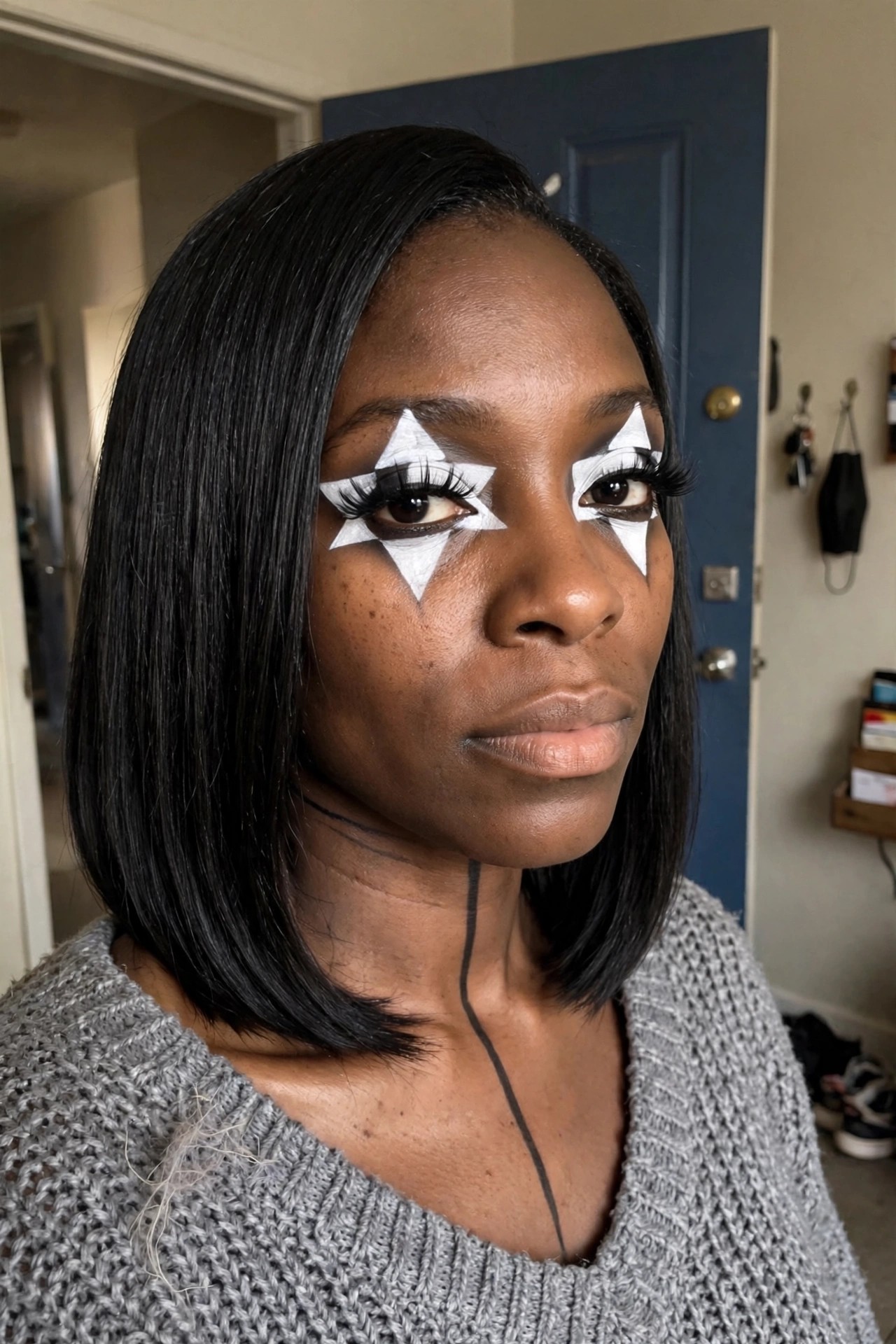 Close up of white star shaped face paint around both eyes with black neck line on a person with dark skin and short black hair.