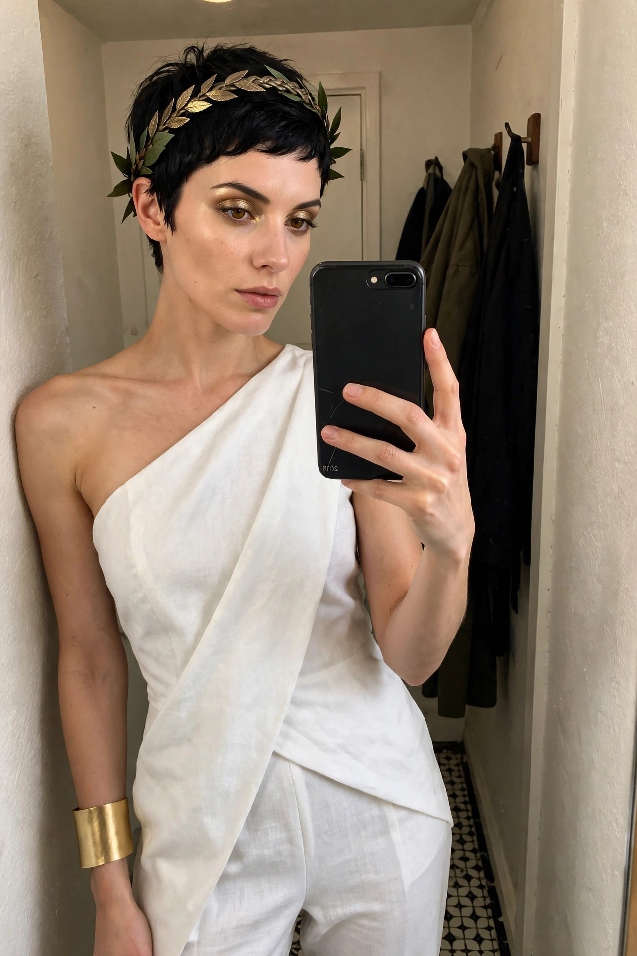 Woman wearing a white one-shoulder draped Greek goddess costume with a gold laurel wreath headpiece and matching gold cuff bracelet.