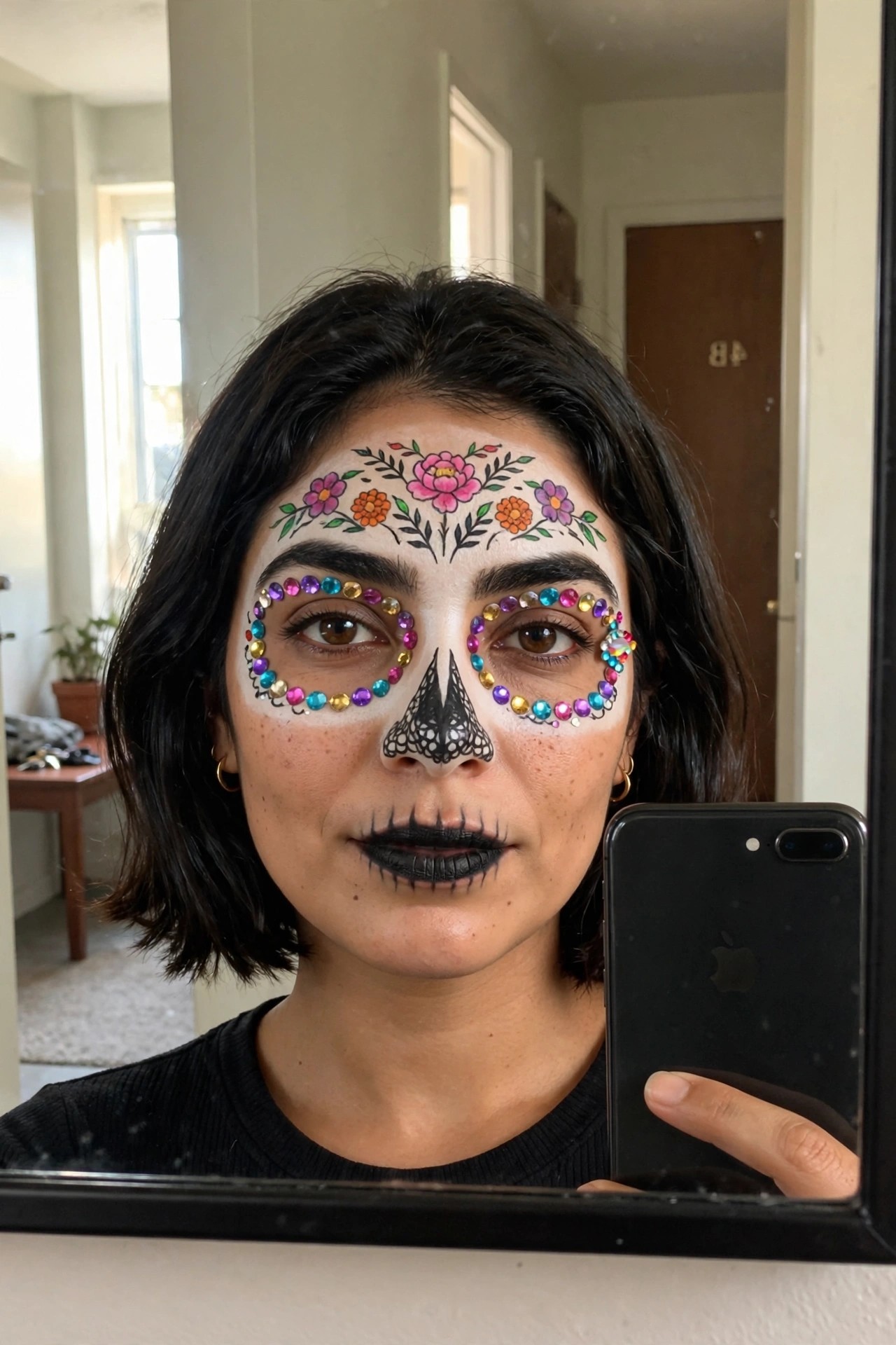 Close up of sugar skull makeup with colorful rhinestones circling the eyes, black nose and mouth paint, and floral designs across the forehead.