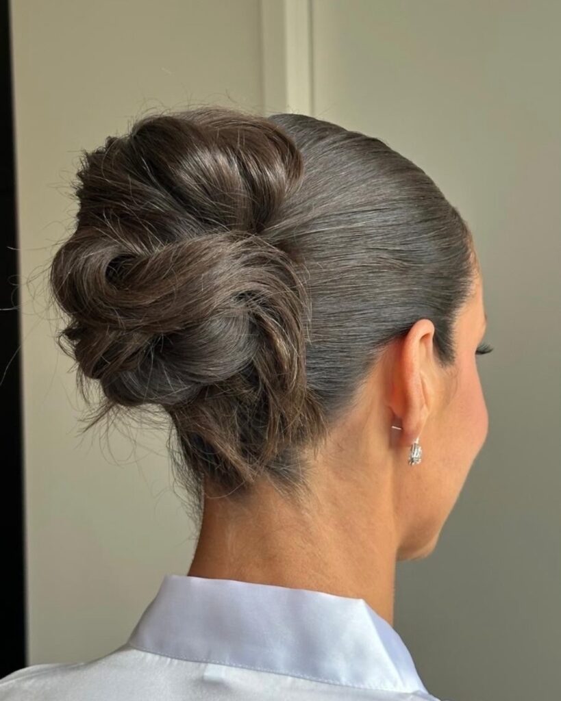A woman with thick brunette hair styled in a sleek low twisted bun at the nape of the neck.