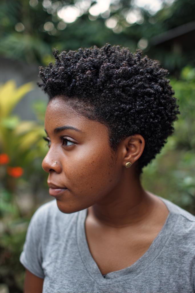 A woman in side profile displaying a short tapered haircut styled with tight, glossy black finger coils.