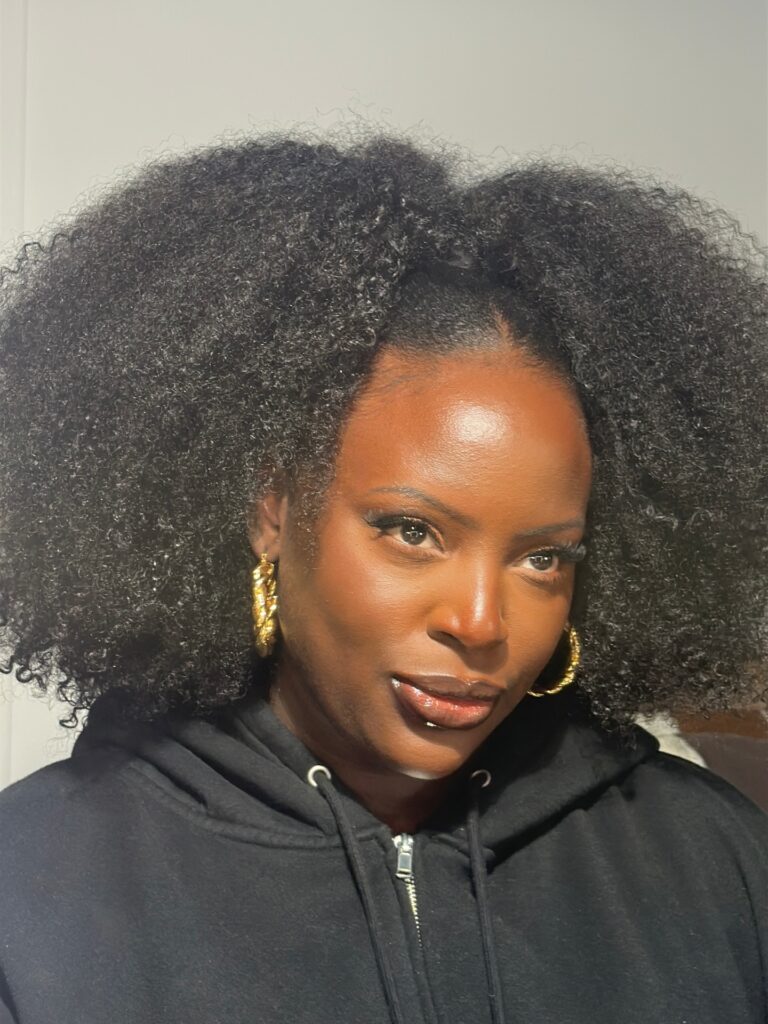A woman with shoulder length dark coily hair wearing a half up ponytail style with gold hoop earrings.