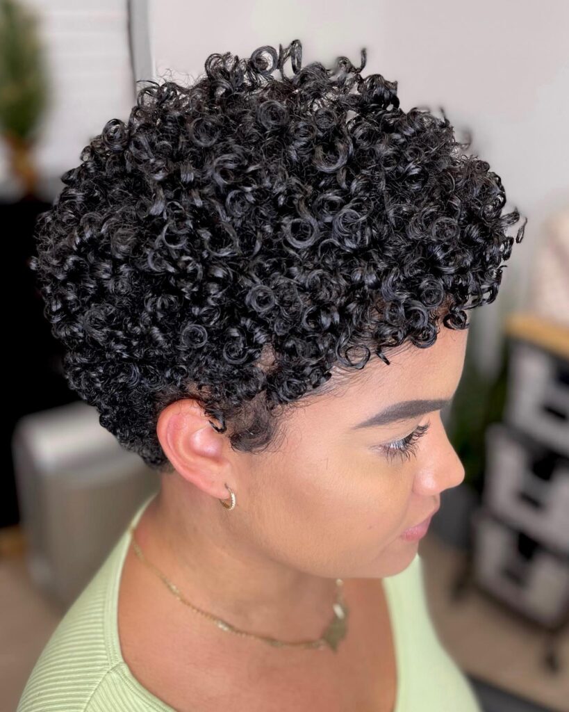 A woman showing off a short, glossy pixie haircut with ultra defined black coily ringlets.
