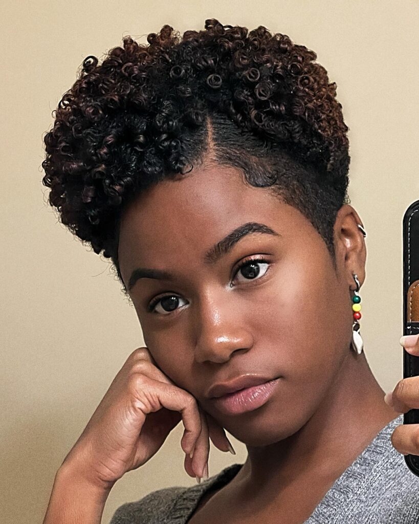 A woman with a short tapered coily haircut featuring a crisp side part and smooth edges taking a selfie.