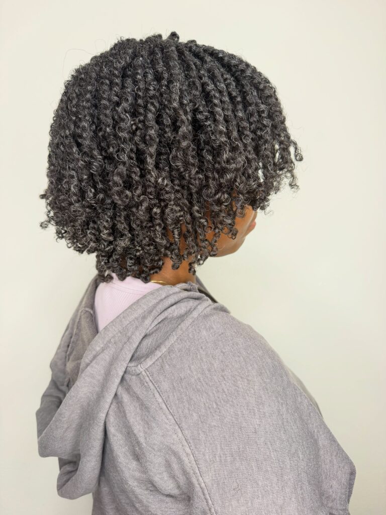 A woman with salt-and-pepper coily hair styled in chin-to-shoulder length spiral twists, seen from the side.