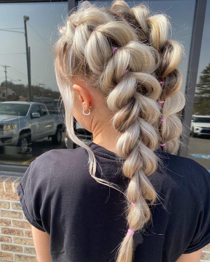 Back view of a woman with long icy blonde hair styled in double bubble braids secured with small pink elastics and loose face-framing strands.