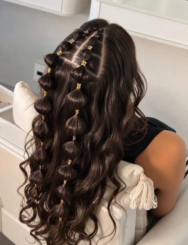  Back view of a woman with very long dark brown wavy hair styled with two rows of bubble ponytails secured with small gold hair cuffs.