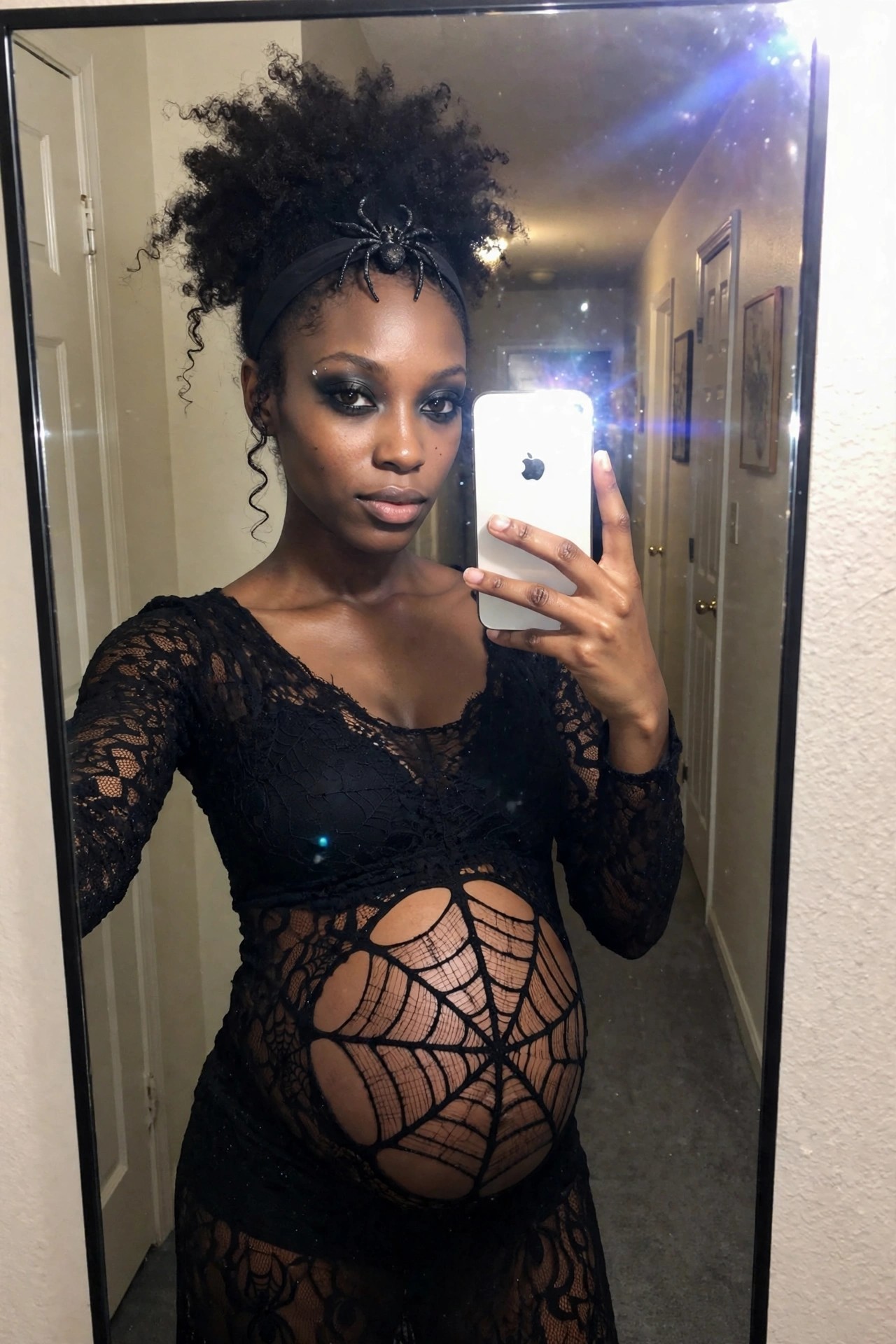 Pregnant woman wearing a black lace dress with large spiderweb cutouts over the belly and a spider headband, taking a mirror selfie.