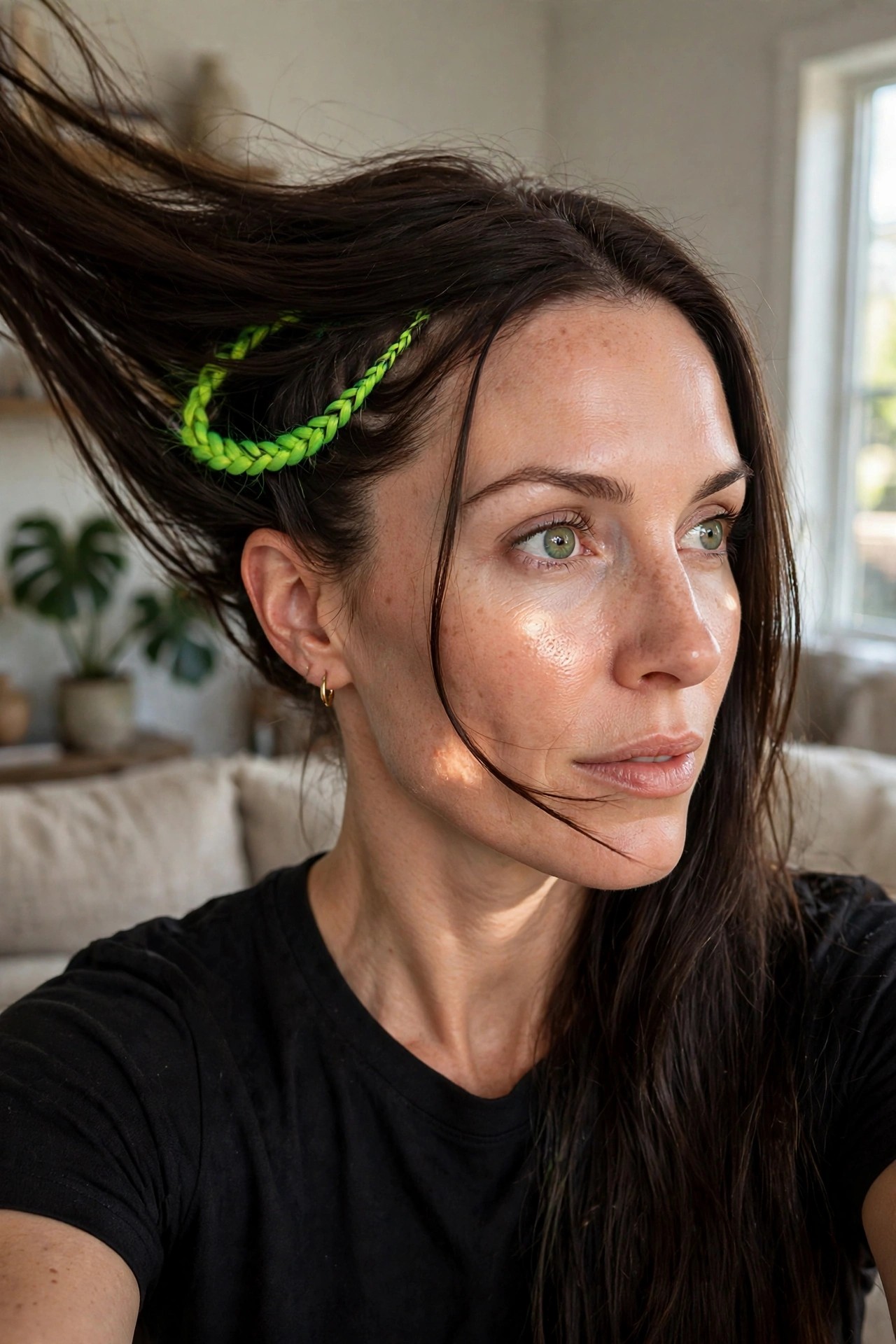 Close-up of long dark hair with a small neon green braid running along the side near the hairline, the rest of the hair loose and slightly windswept.