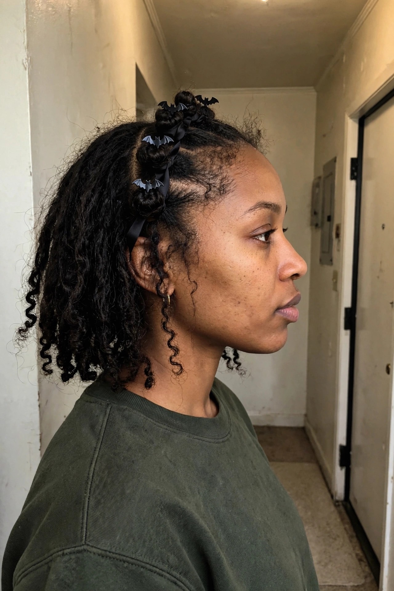 Side profile of curly hair styled with small knotted sections secured by black ribbons and bat shaped clips along the part, loose curls falling below.