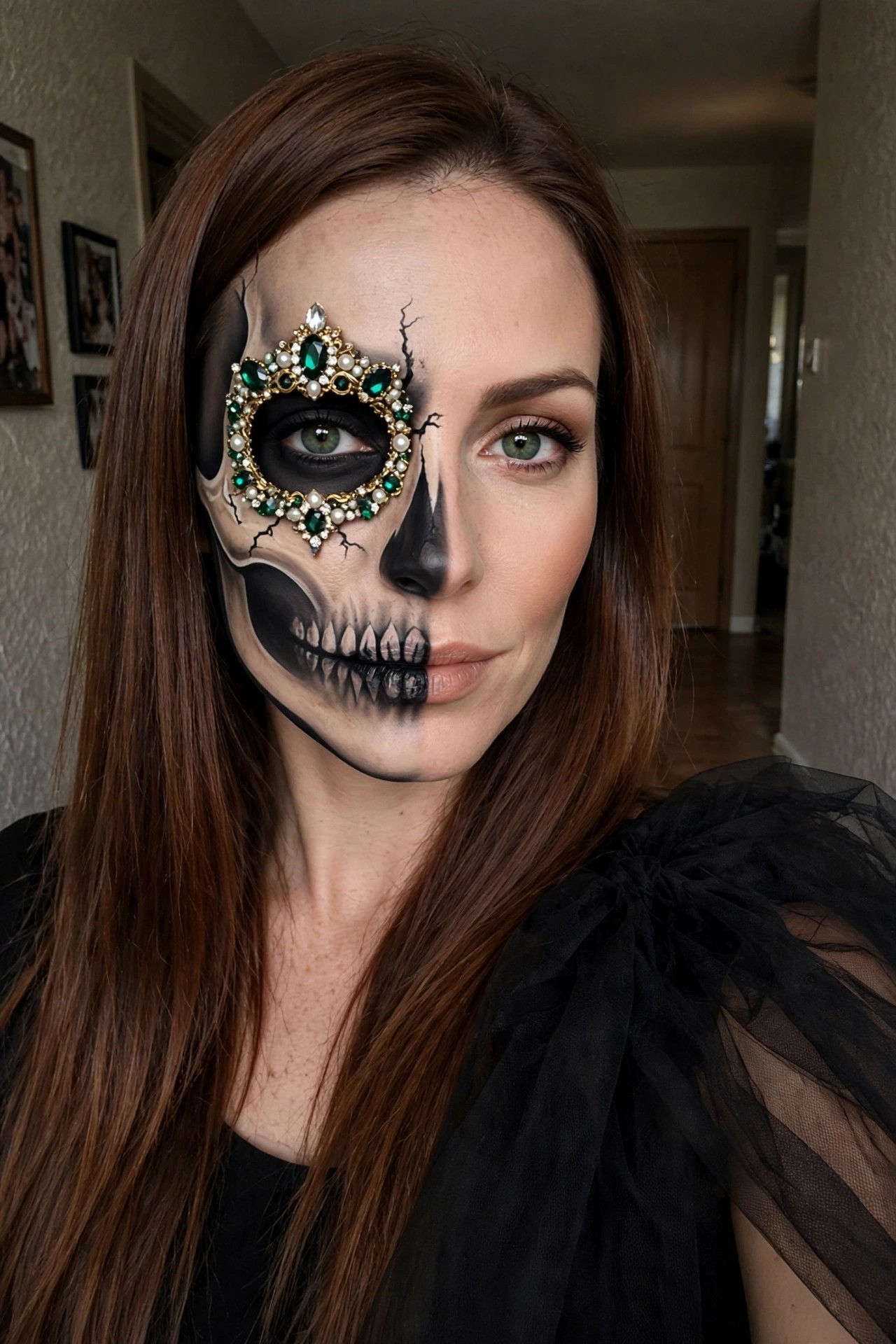 Close up of woman with half face painted as skull showing black eye socket teeth and cracks plus ornate jeweled frame with green gems around left eye.