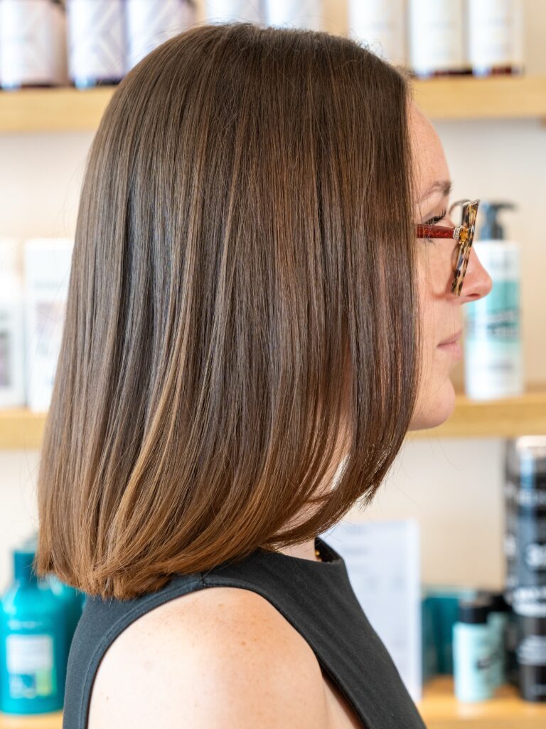 A woman with a sleek, shoulder-length angled brunette lob featuring natural caramel highlights.
