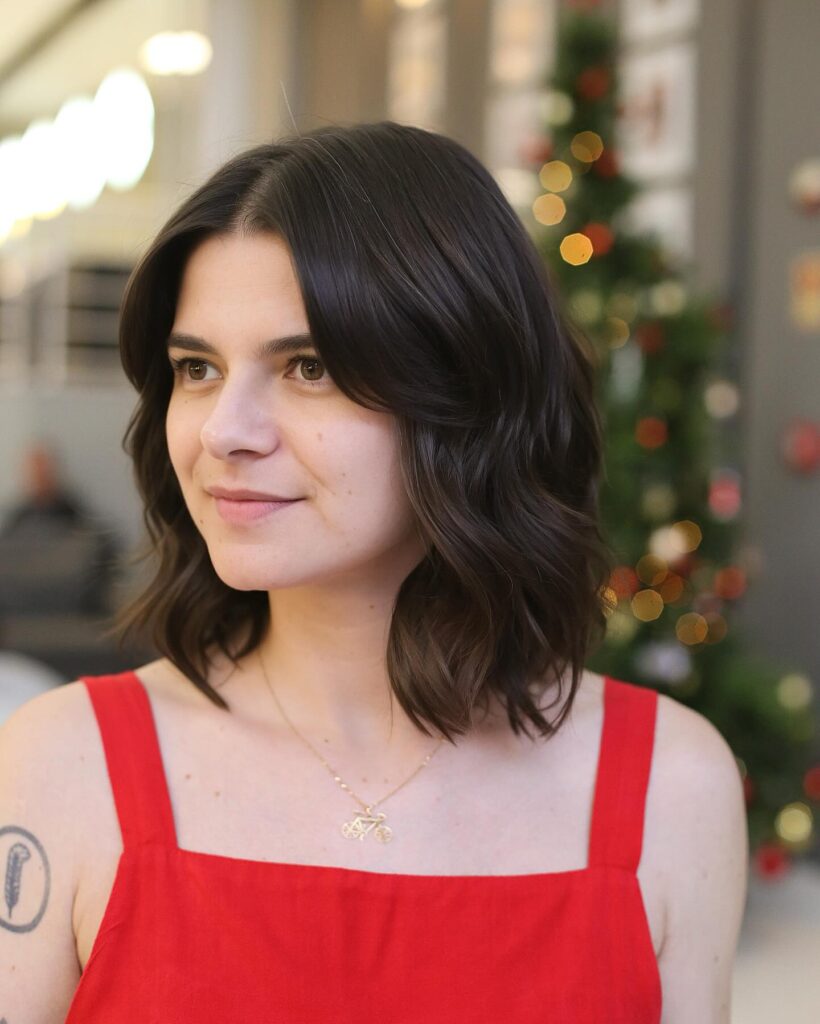 A woman with shoulder-length dark brunette hair styled in loose, beachy waves.