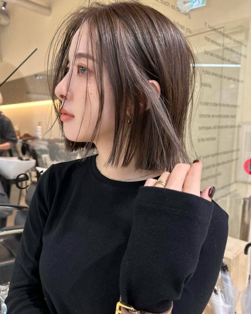 A woman with a shoulder-length ash brown textured bob featuring wispy fringe and piece-y strands.