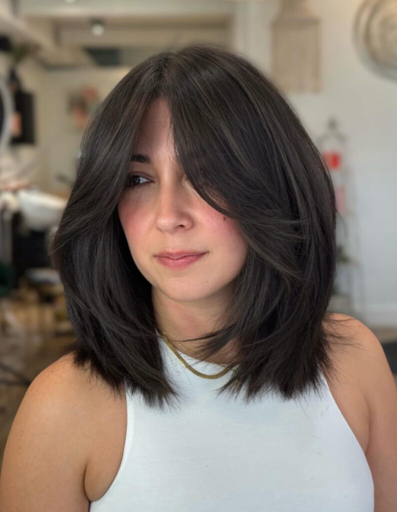 A woman with shoulder-length dark brunette hair featuring feathered layers and a deep side swept fringe.