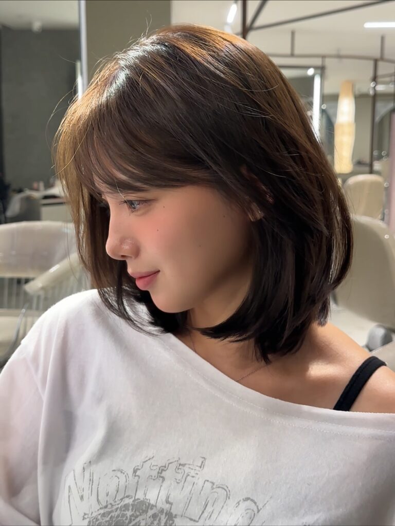 A woman with a shoulder-length choppy layered haircut in deep brown with subtle highlights and a curtain fringe.