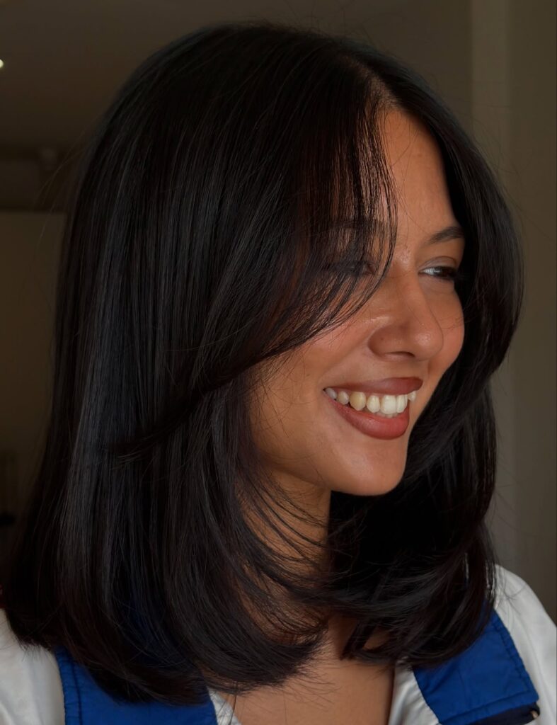 A woman with shoulder-length jet black hair featuring side swept bangs and soft swoopy layers.