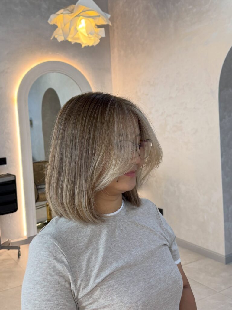 A woman with shoulder-length ash blonde hair featuring curtain bangs and dimensional highlights.