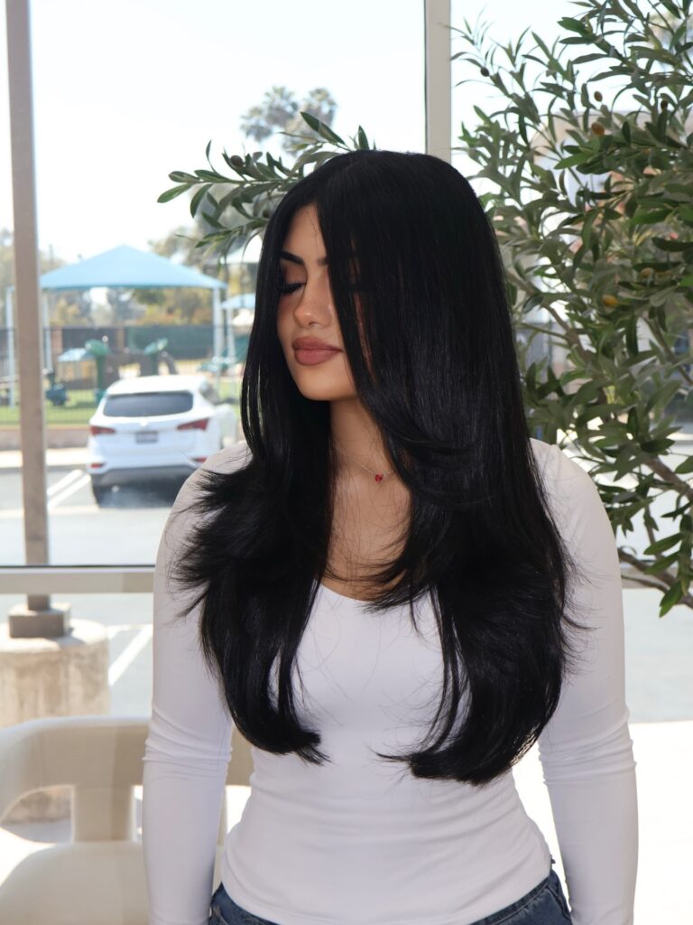A woman with long, sleek jet black hair featuring a center part and feathered flipped layers at the ends.