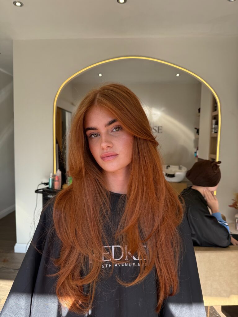 A woman with long, layered copper red hair featuring a natural, piecey texture throughout.