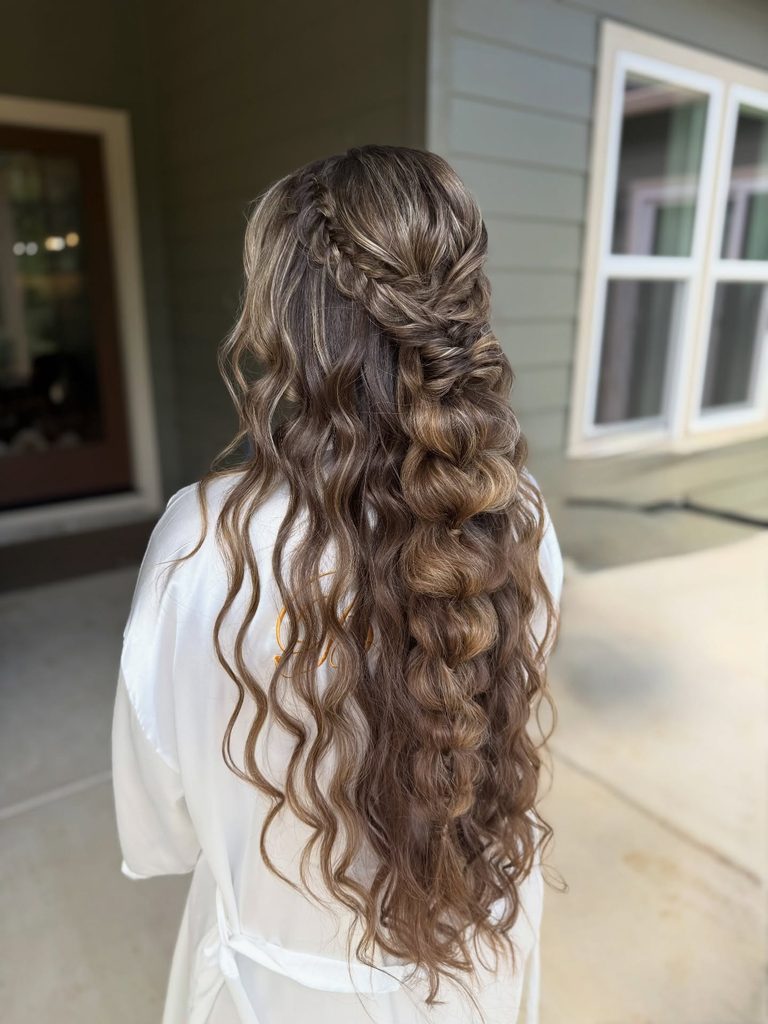 Back view of a woman with very long brunette hair and golden highlights styled in a half up fishtail braid that leads into a bubble braid with loose crimped waves.