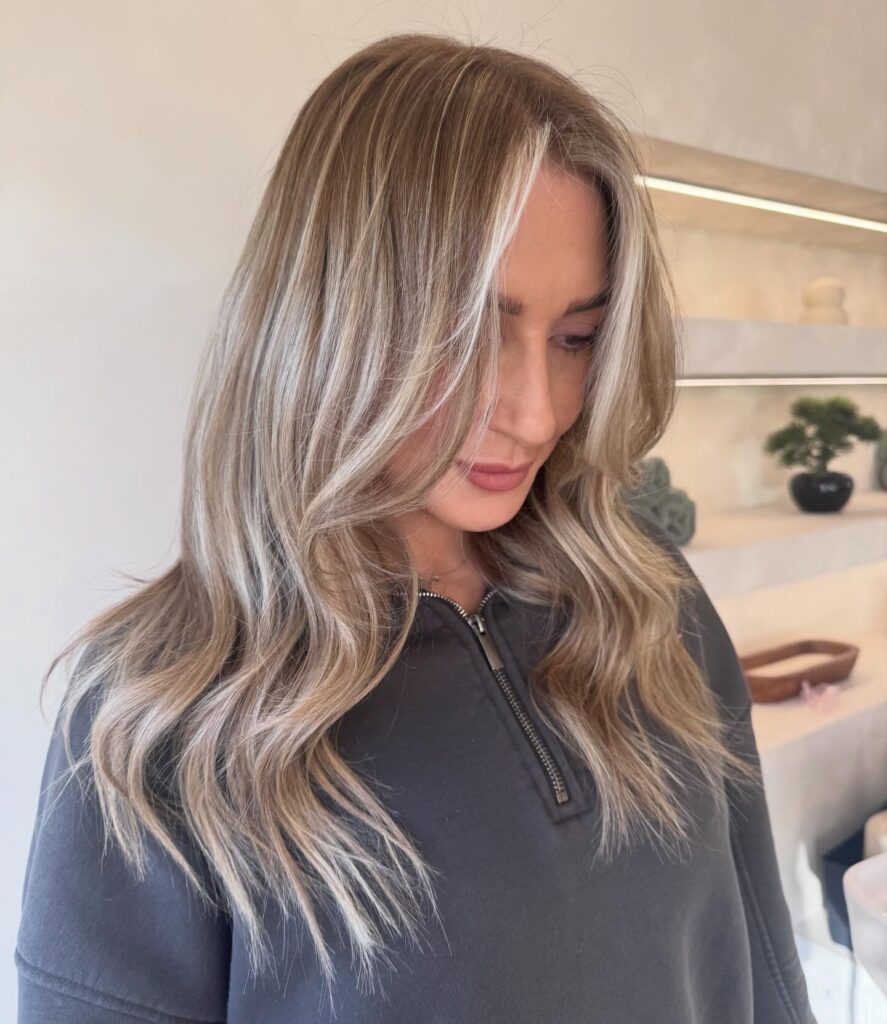 A woman with medium length wavy hair featuring a bright blonde money piece against a darker base.