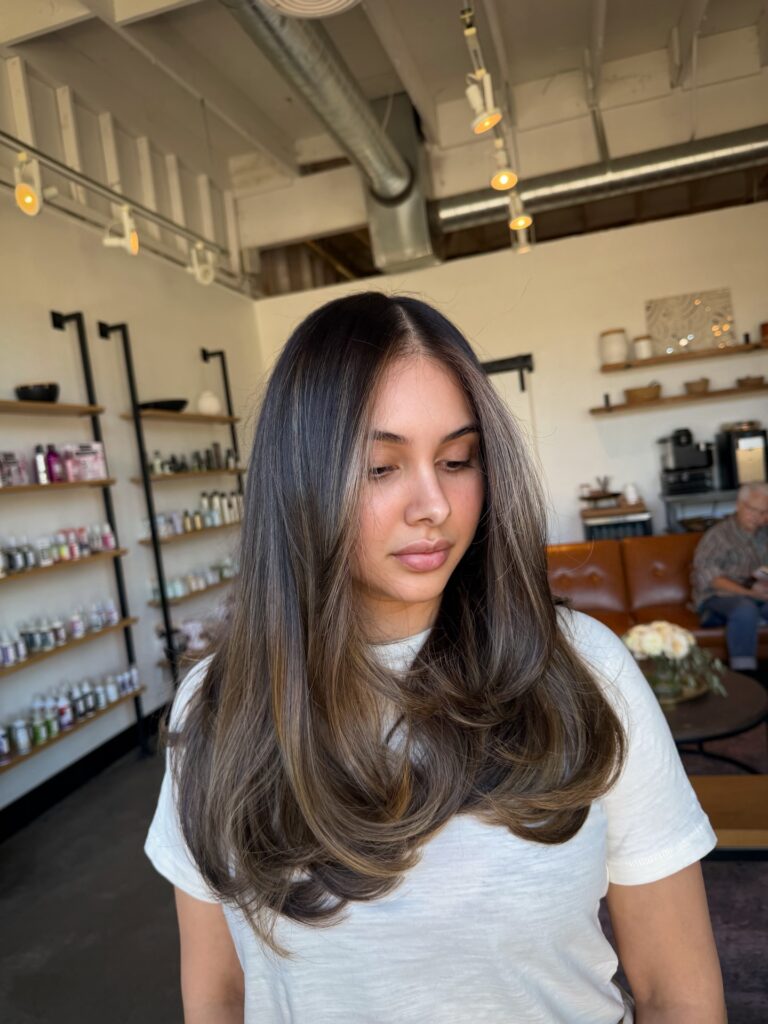 A woman with long, dark brunette hair featuring subtle face-framing highlights and flipped-out ends.