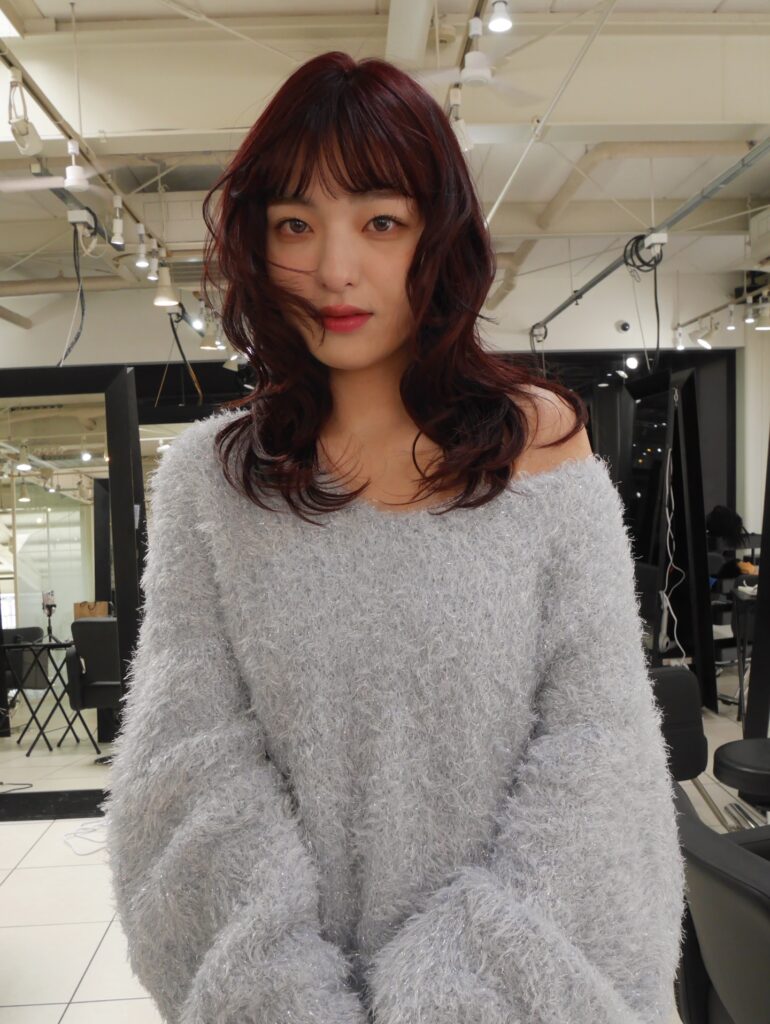 A woman with medium-length cherry red curly hair and full blunt bangs.
