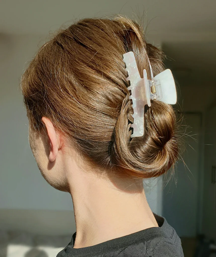 Back view of a woman with caramel brown hair twisted into a low sleek bun secured with a large pearly white claw clip.
