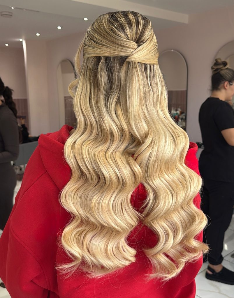 Back view of a woman with extra long golden blonde vintage waves and dark roots styled in a half up criss cross twist at the crown.