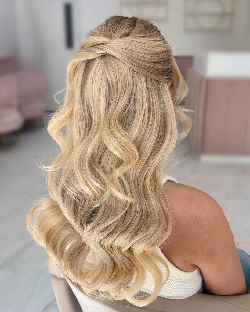 Back view of a woman with long golden blonde hair styled in a crossover twist half up style with big soft curls.
