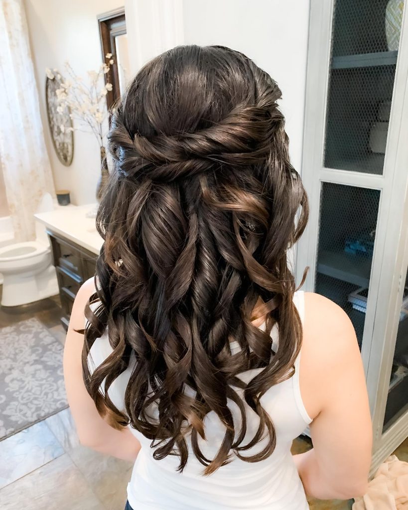 Back view of a woman with long dark brown hair styled in a twisted half up style with big glossy curls cascading down.