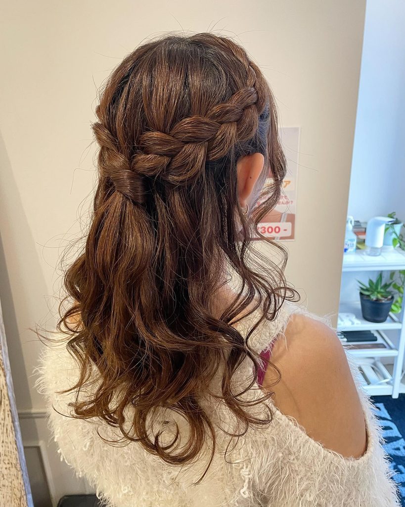 Side view of a woman with long chestnut brown hair styled in a braided crown half up style with loose flowing waves.